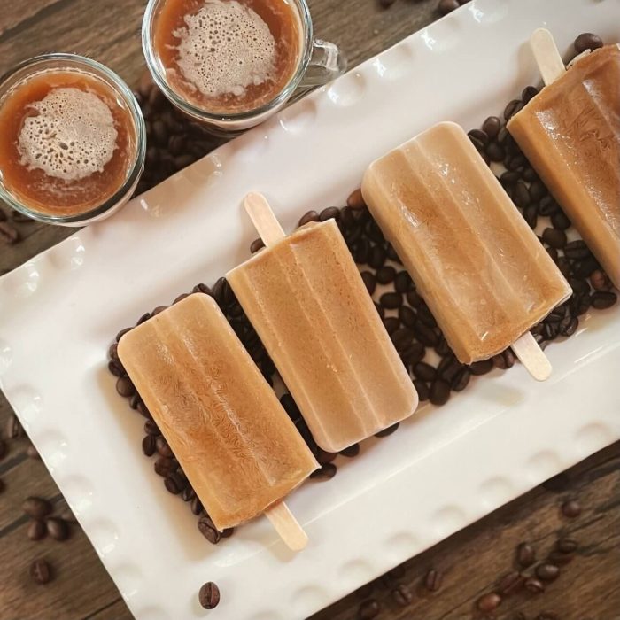 A white plate holds several coffee ice pops, highlighting their smooth surface and deep brown hue.